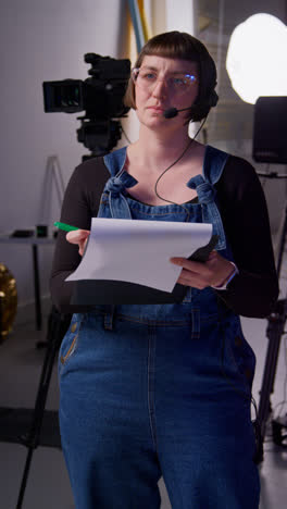 Vertical-Video-Of-Female-Film-Production-Assistant-With-Headset-And-Script-On-Movie-Or-Video-Shoot-In-Studio